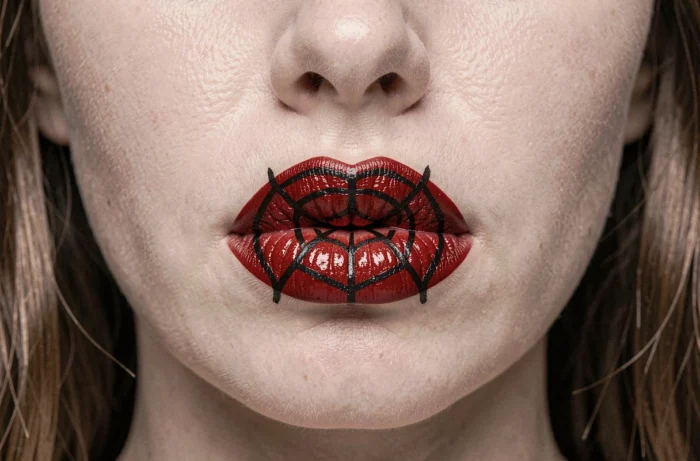 Gros plan sur un maquillage lèvres toile d'araignée avec fond rouge vif et tracés noirs fins formant une toile parfaite sur les lèvres